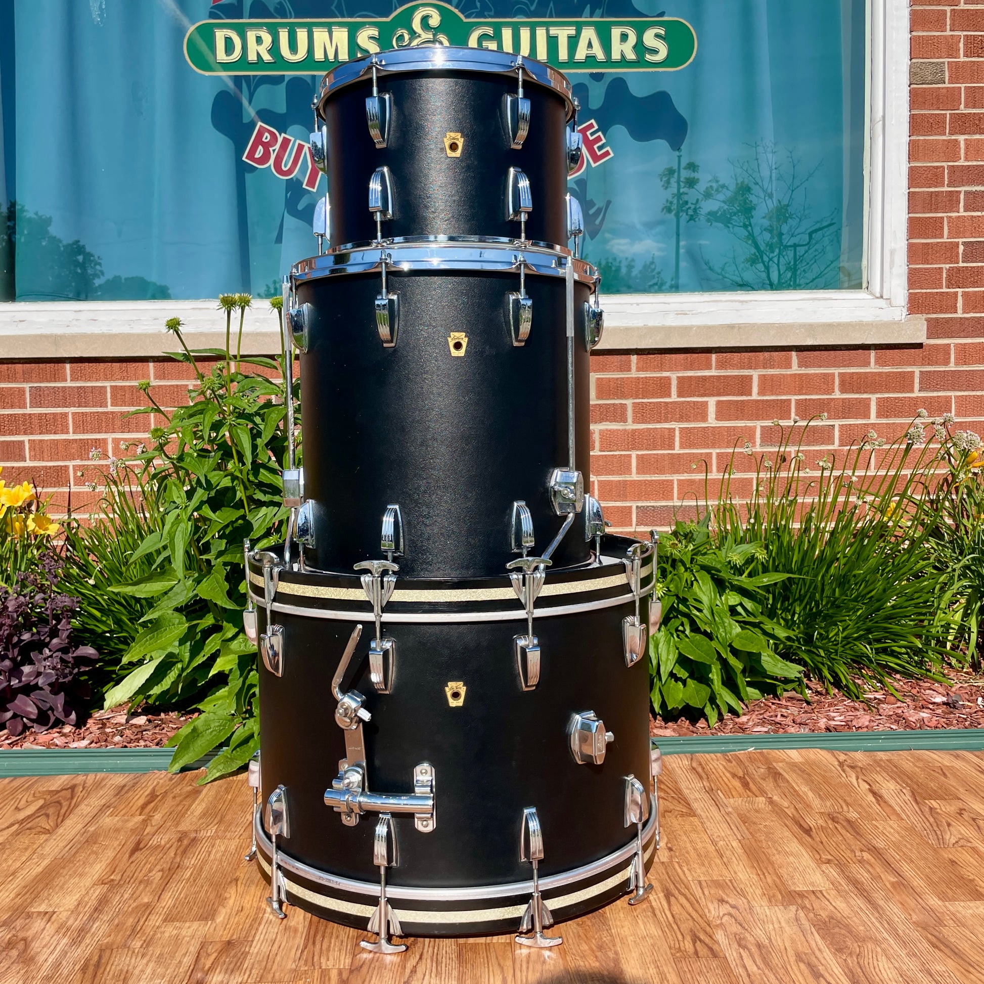 Close, low-angle view of the Ludwig Super Classic kit with the rack tom, floor tom, and bass drum stacked together in front of the Drugan's Drums and Guitars sign